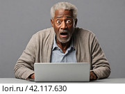 Surprised elderly african american man looking at laptop screen on gray background. Стоковое AI-изображение, AI-художник Васильева Юлия / Фотобанк Лори
