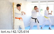 Focused beginner young judo fighter in kimono standing in attacking stance, practicing punches or hand striking techniques as part of kata with group of men. Стоковое видео, видеограф Яков Филимонов / Фотобанк Лори