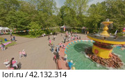 Cherepovets, Russia - May 27, 2023, Families with children at a town festival walk around the fountain in the summer heat. The park is decorated with flags. FPV Aerial Drone Shot. Редакционное видео, видеограф Даниил Хабаров / Фотобанк Лори
