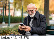Elderly Man Enjoying Serene Time in the Park, Using Smartphone to Stay Connected with the World Around Him. Стоковое AI-изображение, AI-художник Оксана Гильман / Фотобанк Лори