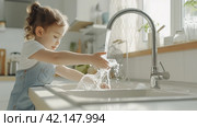 A charming happy little Child is washing dishes in the home Kitchen. The Child has fun helping his parents with the Housework. Стоковое AI-изображение, AI-художник Ирина Ручушкина / Фотобанк Лори