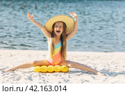 Happy cute smiling little girl in straw hat has fun on the sand on a beach in a swimsuit. Summer concept. Стоковое фото, фотограф Ирина Михайличенко / Фотобанк Лори