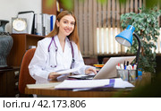 Young woman internist studies the patient's outpatient card, typing the treatment appointment on the computer in the office. Стоковое фото, фотограф Яков Филимонов / Фотобанк Лори
