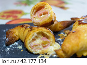A close-up of a flaky, golden-brown pastry with ham and cheese filling, delicious and tasty puff pastry with ham and cheese. Стоковое фото, фотограф carlos l vives / Фотобанк Лори