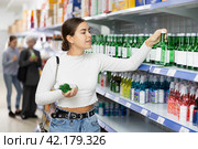 Young girl examining labels on bottles of soju in Asian store. Стоковое фото, фотограф Яков Филимонов / Фотобанк Лори