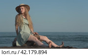 Sensual blonde woman sitting on log on beach of black sand on background of sea waves on sunny day. Стоковое видео, видеограф А. А. Пирагис / Фотобанк Лори