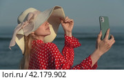 Young woman using smartphone making video selfie on beach on background of ocean waves. Стоковое видео, видеограф А. А. Пирагис / Фотобанк Лори