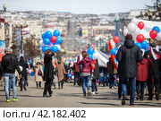 Люди с флагами и воздушными шарами идут по улице во время праздничной первомайской демонстрации. Счастливая женщина фотографирует на смартфон. Праздник весны и труда в России. Магадан, Магаданская область, Россия - 1 мая 2018 года. Редакционное фото, фотограф Андрей Степанов / Фотобанк Лори
