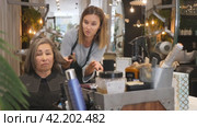 Portrait of young woman professional hair stylist talking to elderly female client in salon, choosing new hairdo. Стоковое видео, видеограф Яков Филимонов / Фотобанк Лори