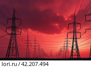Electricity distribution station pylons on background of red acid sky. Silhouette image power line support high voltage power transmission tower and lines in an urban pollution environment. Copy space. Стоковое AI-изображение, AI-художник Aleksandr Golubev / Фотобанк Лори