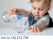 Маленький ребенок наливает воду из бутылки в стакан. Стоковое AI-изображение, AI-художник Щеголева Ольга / Фотобанк Лори