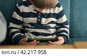 One toddler boy using smartphone sitting in cafe, restaurant. Child looking at mobile phone, modern parenting concept. Lifestyle with digital gadget devices. Bored kid relax with play game on a cell. Стоковое видео, видеограф Марина Демидюк / Фотобанк Лори