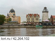 Kaliningrad, Russia - June 20, 2022: Cityscape in rainy day. Synagogue in Kaliningrad on bank of Pregol River and a lighthouse in the Fishing village. Touristic location. Street cafe. tourists walking. Редакционное фото, фотограф YuryKara / Фотобанк Лори