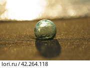 Photography of clear crystal ball lying at the sand of the beach. Golden water and yellow sand as background. Miracle view. Concept of the beauty in nature. Sunny day. Стоковое фото, фотограф YuryKara / Фотобанк Лори