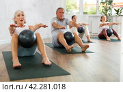 Mature people with young coach sit on karemat, pulled leg to themselves and clamped softball in knee. Стоковое фото, фотограф Яков Филимонов / Фотобанк Лори