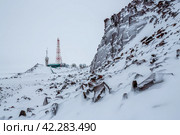 Зимний пейзаж с телебашней, антеннами и спутниковыми тарелками на вершине заснеженной горы. Телекоммуникационная инфраструктура Крайнего Севера России в Арктике. Анадырь, Чукотка, Россия. Стоковое фото, фотограф Андрей Степанов / Фотобанк Лори