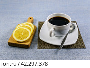 Белая чашка чёрного кофе на салфетке-циновке и лимонные дольки на маленькой разделочной доске. Стоковое фото, фотограф Владимир Устенко / Фотобанк Лори