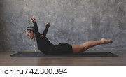 A woman performs exercises to strengthen her back and shoulder muscles, lifts her upper body and legs from a prone position, exercises in black sportswear while lying on a mat. Стоковое видео, видеограф Сергей Чайко / Фотобанк Лори