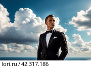 Pensive stylish man in tuxedo and bow tie posing at cloudy sky, thought looking away. Portrait of confident fashionable young guy businessman in tux, luxury image James Bond style. Copy ad text space. Стоковое AI-изображение, AI-художник Aleksandr Golubev / Фотобанк Лори