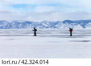 BAIKAL LAKE, KHARANTSY VILLAGE, IRKUTSK REGION, RUSSIA -  March 02, 2024: Tourists travel on skates on the ice of frozen Lake Baikal on a cold winter day. Outdoor activities. Редакционное фото, фотограф Виктория Катьянова / Фотобанк Лори