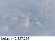 Вид с воздуха на заснеженные горы и облака. Зимний горный пейзаж. Ичигемский хребет, Колымское нагорье. Магаданская область, Сибирь, Дальний Восток России. Отлично подходит для фона. Стоковое фото, фотограф Андрей Степанов / Фотобанк Лори