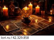 Tarot cards on the table with burning candles, ancient books and amulets. Стоковое AI-изображение, AI-художник Виктория Тельминова / Фотобанк Лори