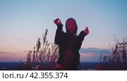 A young girl dancing in the grass against the background of the evening sky. Стоковое видео, видеограф Strunov David / Фотобанк Лори