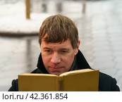 Handsome man in Moscow city center during coronavirus pandemic. New Year holidays. He sitting at the bench and reading the book in the public park. Стоковое фото, фотограф YuryKara / Фотобанк Лори