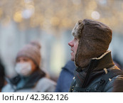 Handsome man walking in Moscow city center. Cold winter in the Russian capital during coronavirus pandemic time. He wear hot cap made of natural sheepskin. It fastened at the chin to protect from cold. Стоковое фото, фотограф YuryKara / Фотобанк Лори