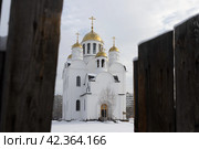 Храм Преображения Господня, город Братск, Иркутская область, Россия. Восточная Сибирь. Вид через проход в заборе на большую красивую белую церковь. Строительство православной церкви в сибирском городе. (2024 год). Стоковое фото, фотограф Андрей Степанов / Фотобанк Лори