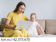 Curious child looking at mother laptop display. Mother using gadgets for baby entertainment. Стоковое фото, фотограф Natalia Gdovskaia / Фотобанк Лори