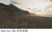Drone flight over endless sand beach Cofete. Volcanic mountain landscape. Golden sandstones in sunset warm light. Ocean water evaporation. Dust, mist, fog rises above the waves. Fuerteventura Island. Стоковое видео, видеограф Igor Tichonow / Фотобанк Лори
