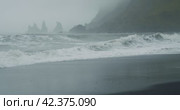 The black sand beach of Reynisfjara with waves hitting the shore on foggy rainy stormy day Vik, Iceland. Стоковое видео, видеограф Igor Tichonow / Фотобанк Лори