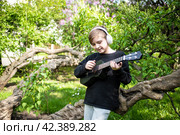 10 летний мальчик играет на черной укулеле, маленькой гавайской гитаре на природе, в парке, на фоне цветущей сирени. Стоковое фото, фотограф Яна Проничева / Фотобанк Лори
