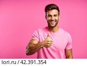 Young man at pink background showing gesture up, very happy and excited, looking at camera. Guy in t-shirt with sign good, smiling and thinking for success. Winning concept. Copy text space. Стоковое AI-изображение, AI-художник Aleksandr Golubev / Фотобанк Лори