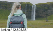 Iceland outdoor trip Woman with backpack near Seljalandsfoss waterfall. Стоковое видео, видеограф Igor Tichonow / Фотобанк Лори