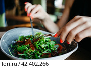 A girl eats arugula salad from a beautiful plate in a restaurant, hands with a fork and knife. Стоковое фото, фотограф Александра Баранова / Фотобанк Лори