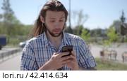 Front view of a perplexed man with a small beard walking checking smart phone content. Стоковое видео, видеограф EStarodubov / Фотобанк Лори
