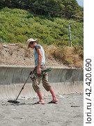 A man wearing shorts and a hat, with a metal detector, is searching for gold and coins on a sandy beach the daytime in summer. Стоковое фото, фотограф Светлана Семёновская / Фотобанк Лори