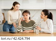 Sad woman sits silently in kitchen, adult girls sympathize and comfort her. Стоковое фото, фотограф Яков Филимонов / Фотобанк Лори