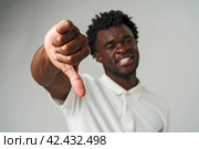 Young African Man Giving Thumbs Down Gesture Against a Neutral Background. Стоковое фото, фотограф Сергей Толмачёв / Фотобанк Лори