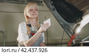 Автосервис. Attractive female mechanic checking oil in the engine in garage workshop. Стоковое видео, видеограф EStarodubov / Фотобанк Лори