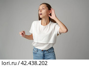 Young woman listening with her hand on an ear on gray background. Стоковое фото, фотограф Сергей Толмачёв / Фотобанк Лори