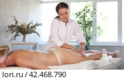 Focused professional young masseuse performing anti-cellulite thigh and butt massage to female client in spa center. Стоковое видео, видеограф Яков Филимонов / Фотобанк Лори