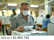 Businessman in glasses and mask reading document in modern office. Стоковое AI-изображение, AI-художник Юрий Поздников / Фотобанк Лори