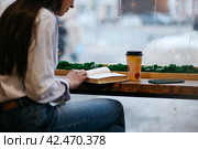 Brunette girl in a cafe drinking coffee, reading a book, close up. Стоковое фото, фотограф Александра Баранова / Фотобанк Лори