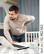 Man experiencing severe back pain after working long hours on laptop. Стоковое фото, фотограф Яков Филимонов / Фотобанк Лори