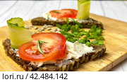 Rye bread bruschettas with cottage cheese on a wooden kitchen board are decorated with vegetables and herbs. Стоковое фото, фотограф Ярославский Максим / Фотобанк Лори