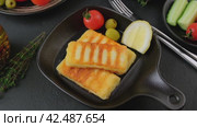 Grilled halloumi cheese in a black pan with olives, tomatoes, cucumbers, thyme and lemon. Traditional cheese of the Eastern Mediterranean. Black background, selective focus, close-up. Slow motion. Стоковое видео, видеограф Наталья Любина / Фотобанк Лори