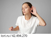 Young woman listening with her hand on an ear on gray background. Стоковое фото, фотограф Сергей Толмачёв / Фотобанк Лори